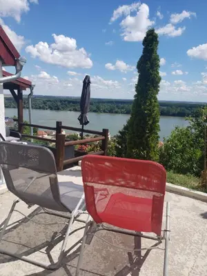 two chairs and an umbrella on a patio overlooking a river at Vila Slankamenka in Stari Slankamen
