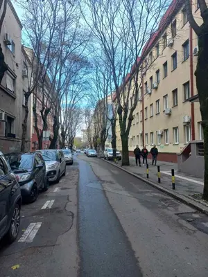 two people walking down a city street with parked cars at Donji Grad in Belgrade
