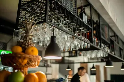 a bar with glasses hanging above a counter with a man at Hotel GardeNN in Belgrade