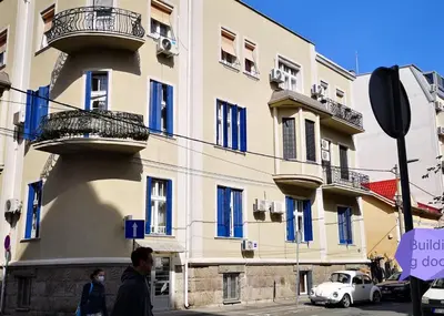 a building with blue windows and a white car on a street at Bibi's apartment in Belgrade