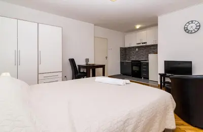 a white bedroom with a large bed and a kitchen at Apartman Pionir in Belgrade
