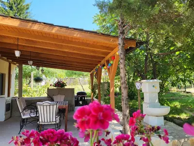a covered patio with a table and chairs and pink flowers at Vila Mila Fruška Gora in Velika Remeta
