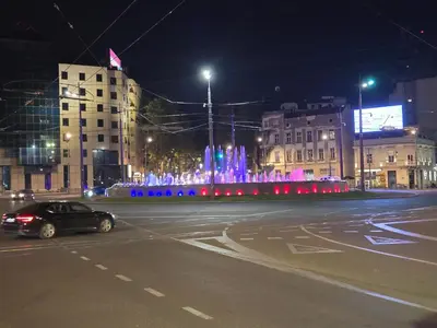 a car driving down a street with a fountain at night at Angelina 03. in Belgrade