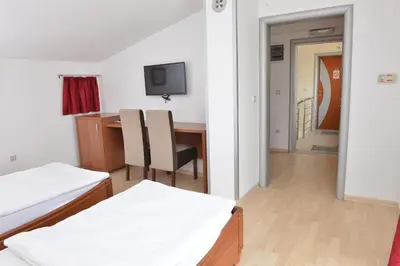 a room with two beds and a desk and a television at Apartment and Rooms In Club in Inđija