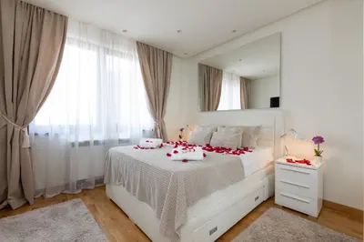 a white bedroom with a large white bed with red pillows at Belgrade Waterfront Apartments - River View in Belgrade