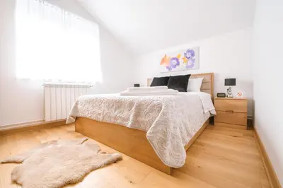 a white bedroom with a large bed and a rug at Afrodita apartman in Surčin