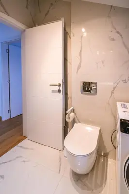 a white bathroom with a toilet and a door at Mikonos apartman in Surčin