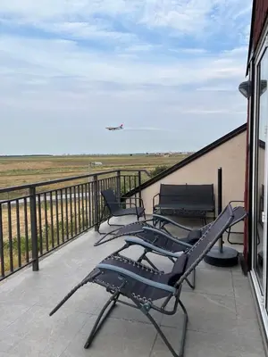 a balcony with chairs and an airplane flying in the sky at Airport Gate 25 in Ledine