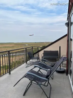 a balcony with chairs and an airplane in the sky at Airport Gate 25 in Ledine