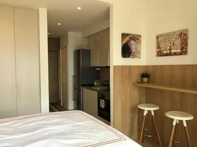 a bedroom with a bed and a kitchen with stools at Cozy Belgrade Waterfront studio with Murphy bed in Belgrade