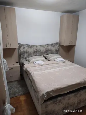 a bedroom with a bed with white sheets and wooden cabinets at Stan na dan in Resnik