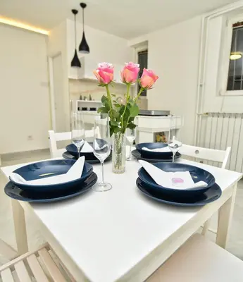 a white dining room table with blue plates and pink roses at Alexandar13 in Belgrade