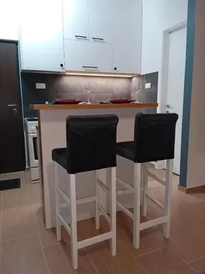 a kitchen with two bar stools and white cabinets at Apartman KLM in Pančevo