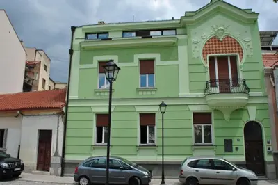 a green building with two cars parked in front of it at Globetrotter's City Center Pied-à-Terre ᯤ in Belgrade