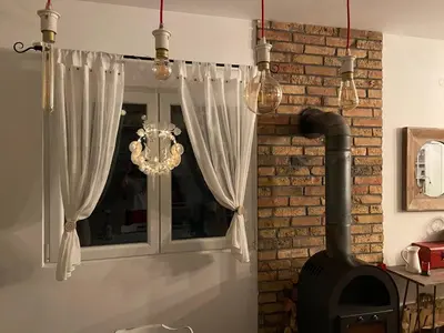 a fireplace with white curtains and a chandelier at Kućica in Velika Remeta