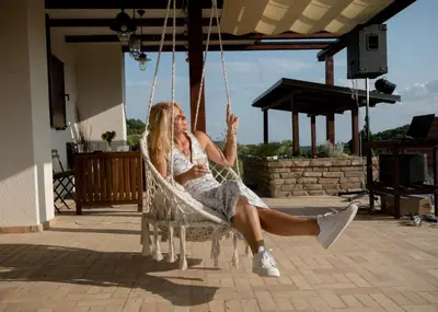 a woman sitting in a swinging chair on a patio at Kućica in Velika Remeta