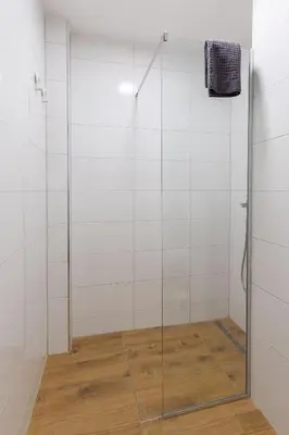 a shower with a glass door and a wooden floor at Siva in Fontana