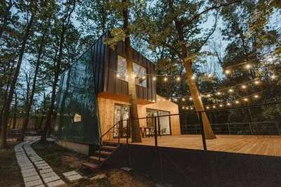 a house in the woods with lights on a deck at Studio Žbun - Kuća na Avali in Pavi°evac