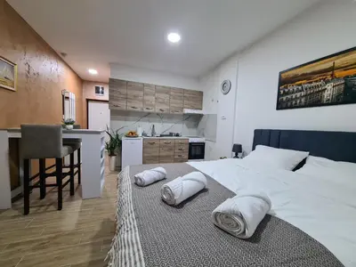 a bedroom with a large white bed and a kitchen at Stella Apartman Ruma in Ruma