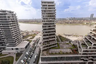 a tall building with a parking lot next to a river at Huge 3 Bedroom Apartment With River View in Belgrade