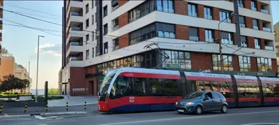 a red bus driving down a street with a small car at APARTMAN FLORENCE in Mirijevo